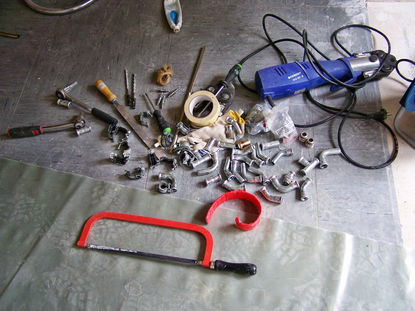 Persgereedschap, fittingen en leidingmateriaal op de vloer